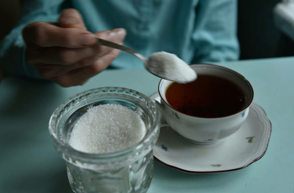 A person spoons a large serving of sugar into a cup of coffee, wondering if it will cause dementia.