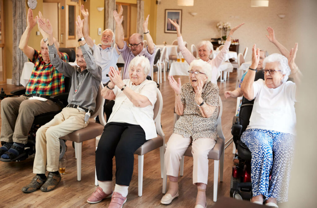 A group of seniors in a senior living facility smiling and clapping their hands in unison.