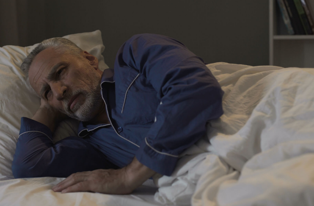 A senior man in his sleepwear lying down in his bed having trouble falling asleep.