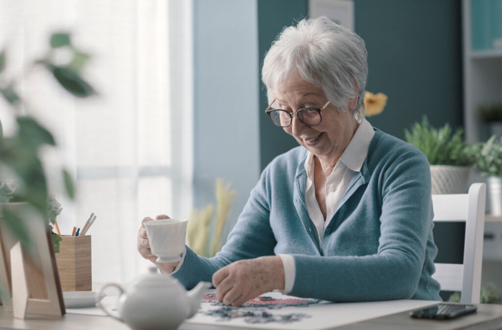 A senior woman solving a jigsaw puzzle while enjoying a cup of tea.
