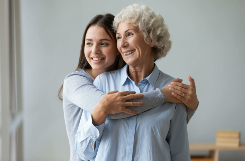 A caring young woman hugging her senior mother while both is looking at a distance.